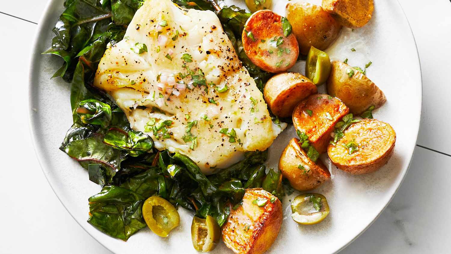 Sheet Pan Cod and Potatoes Served With Greens on a White Plate