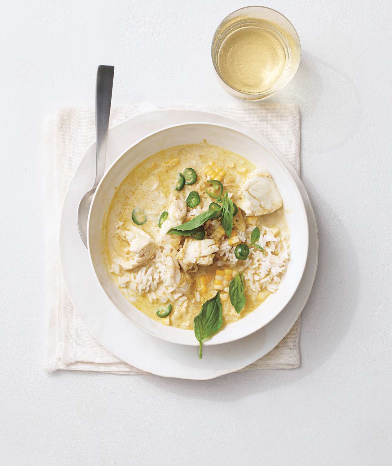 Green Curry With Halibut and Corn Served in a White Bowl With a Metal Spoon