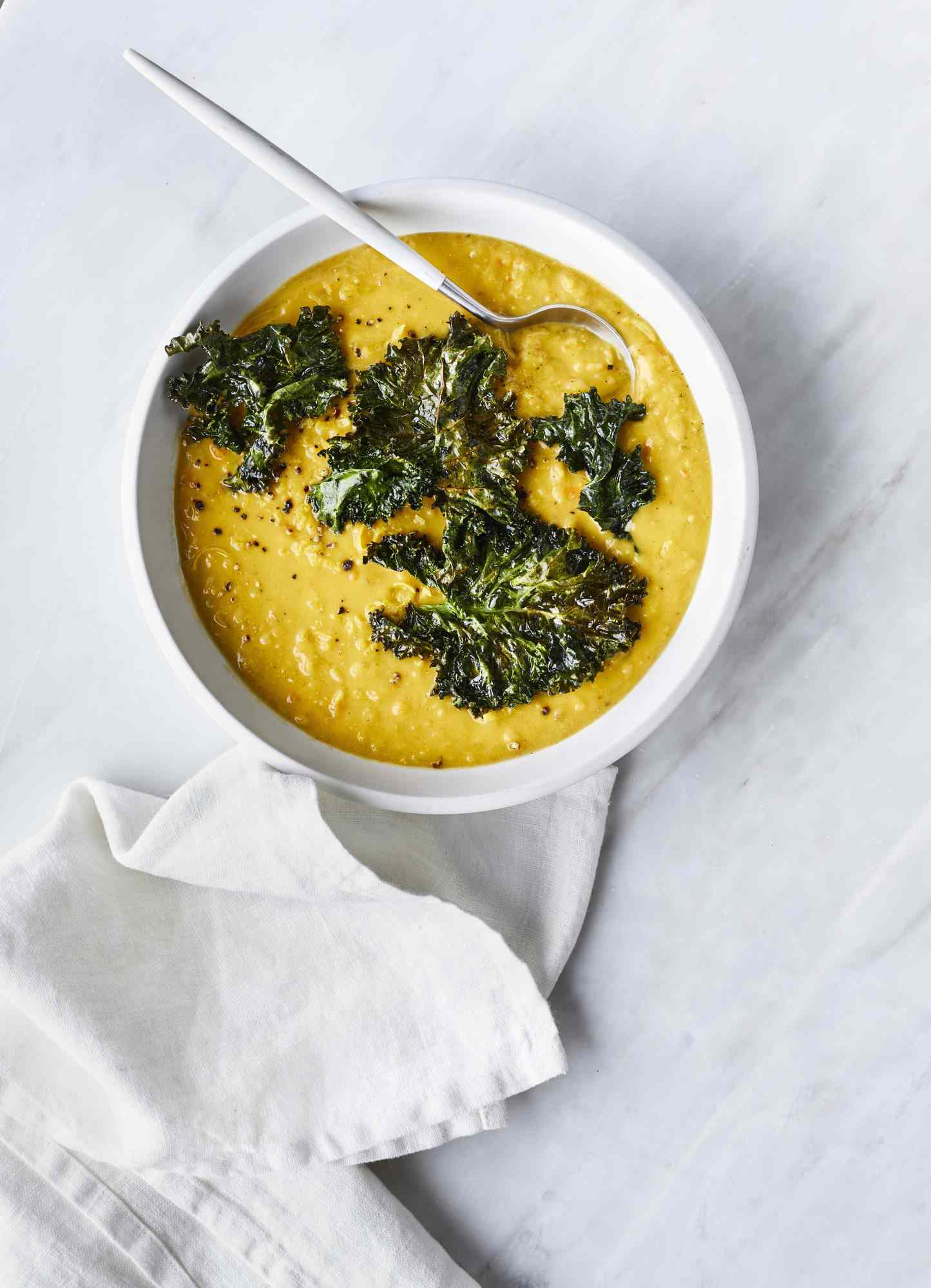 Lemony Lentil Soup, Topped With Kale and Served in a White Bowl With a Metal Spoon