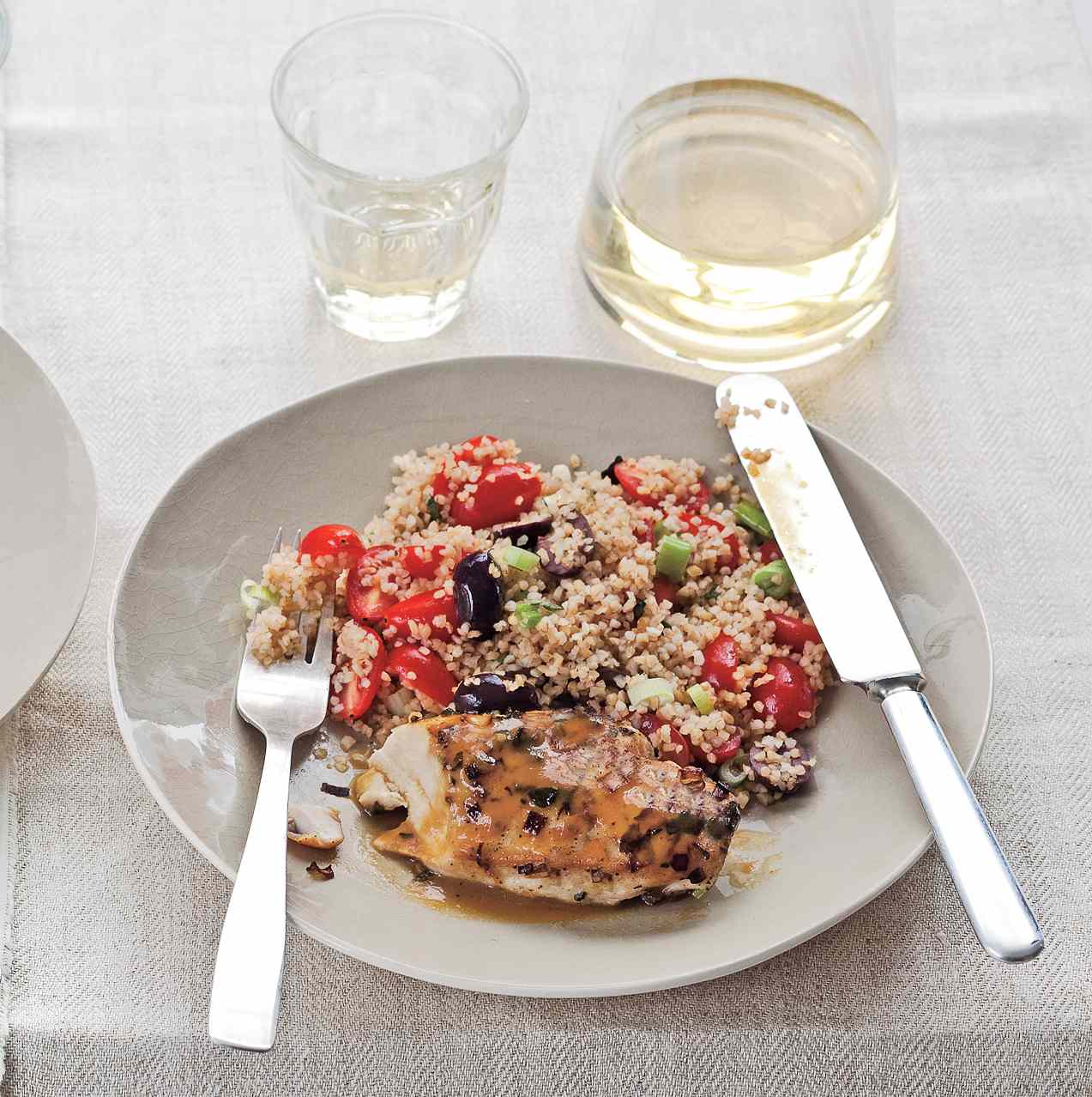 Orange Chicken With Bulgur Pilaf on a White Plate Served With Water and Metal Utensils for Eating