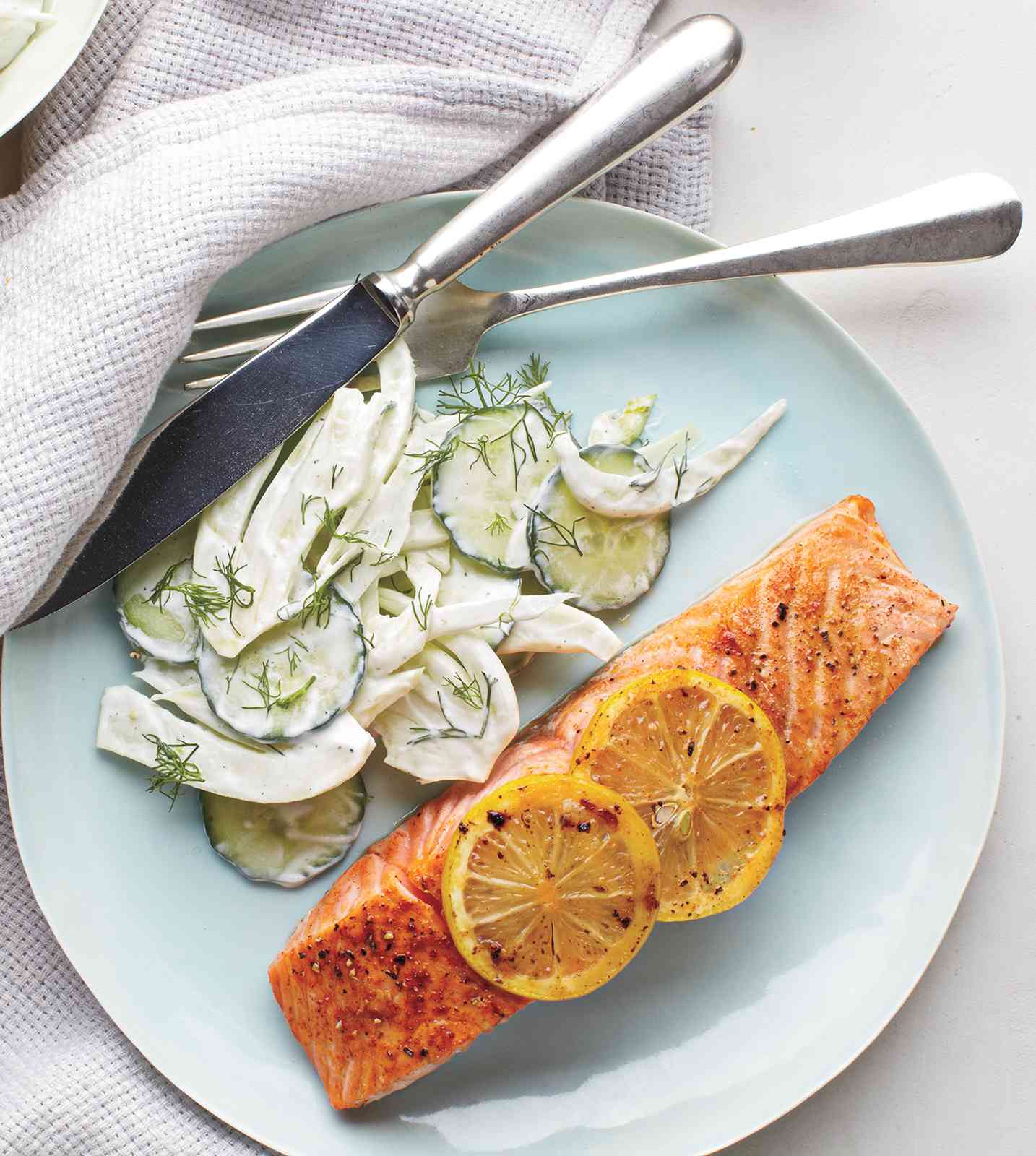 Salmon With Creamy Cucumber-Fennel Salad Served on a Plate With Metal Utensils and a White Cloth Napkin